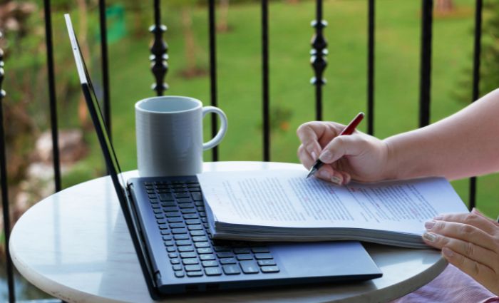 person sitting at a table with a computer proofreading a document