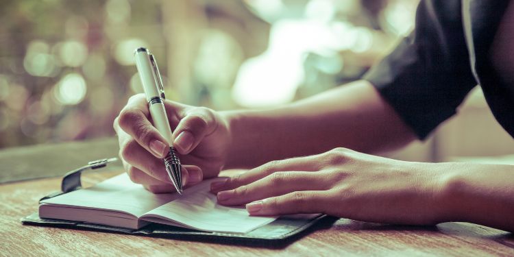 person writing in a journal at a desk